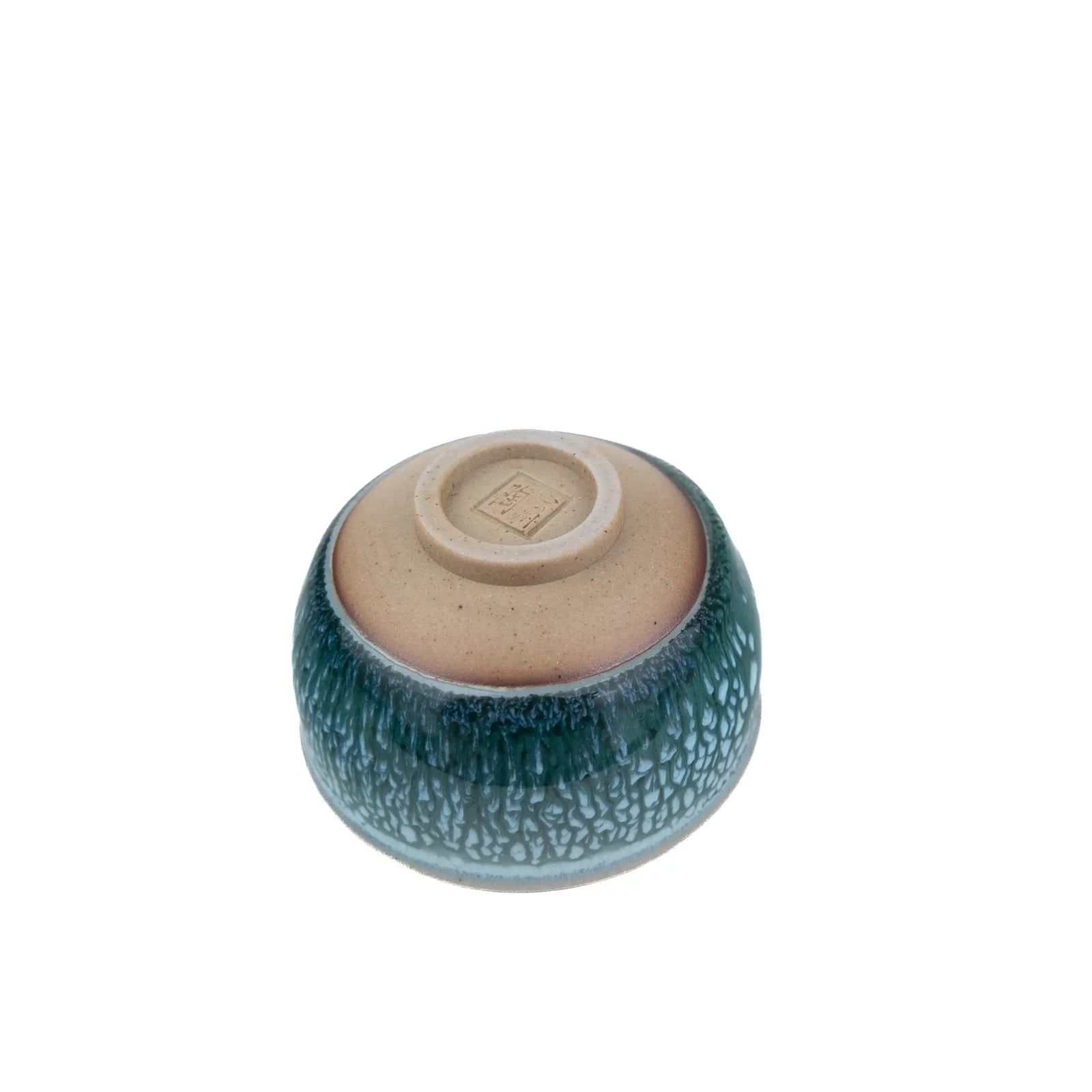 A small ceramic teacup with a textured, crackled glaze in deep teal-green and light blue, featuring a contrasting matte beige interior visible from the bottom.