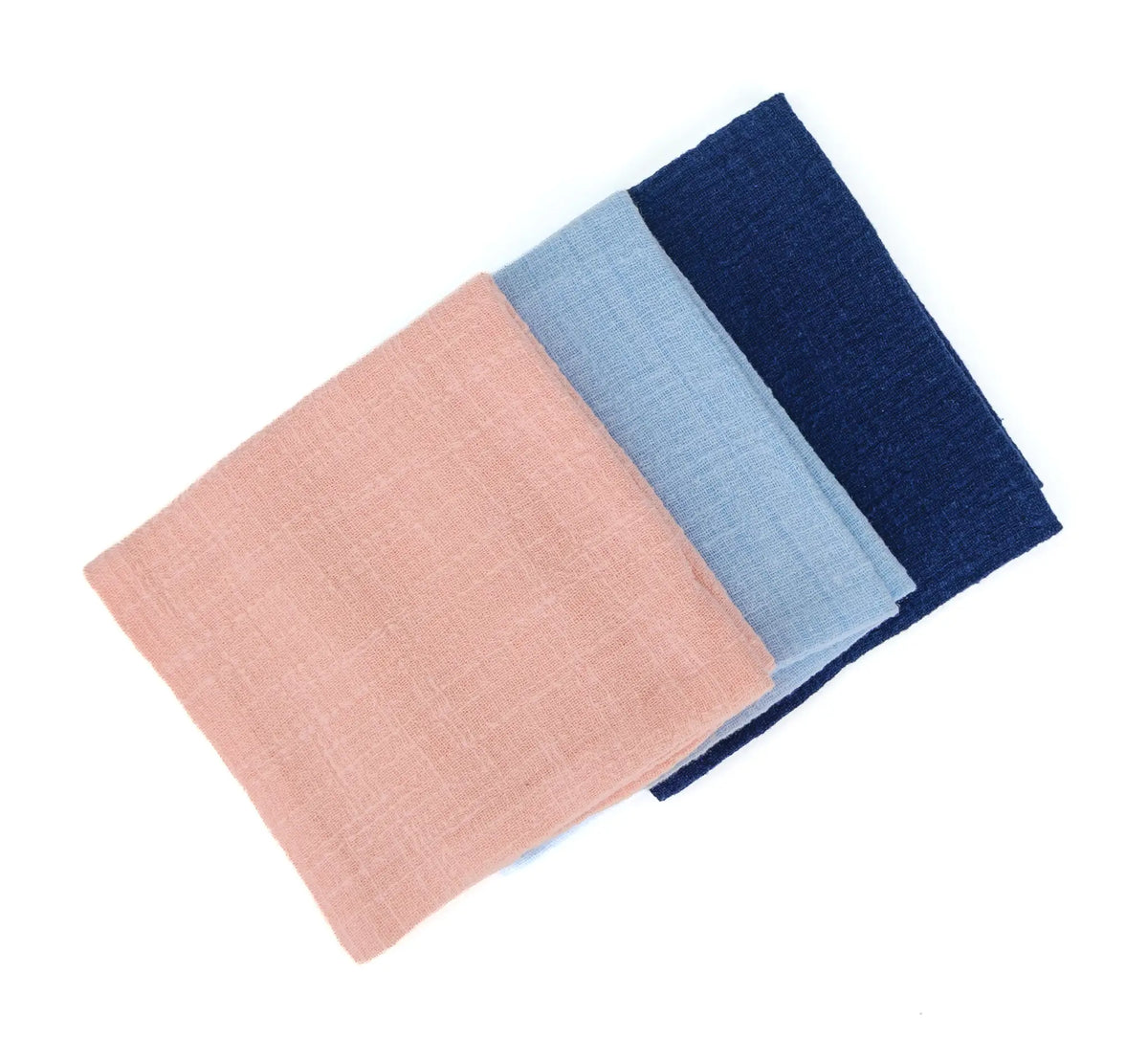 Three different colored linen tea towels folded in squares and placed diagonally across a white background
