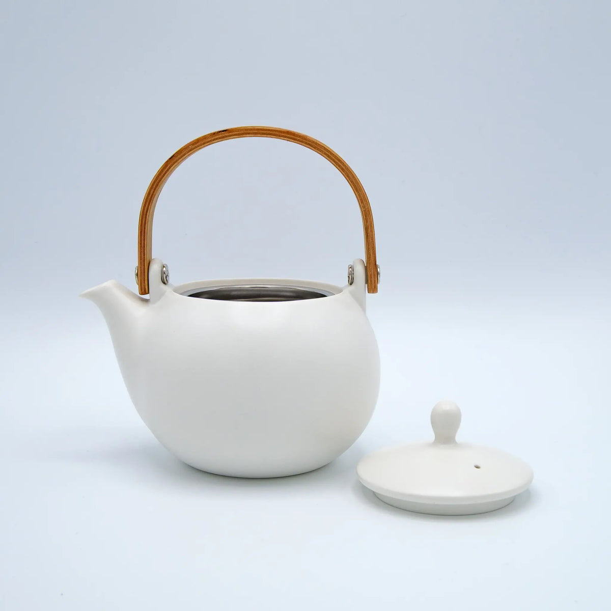 White ceramic teapot with a wooden handle on a light gray background