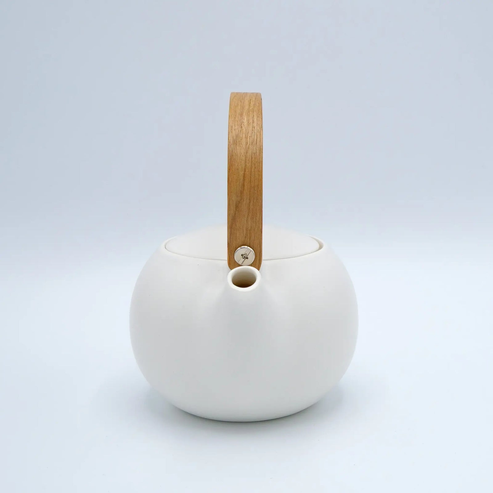 White ceramic teapot with a wooden handle on a light gray background