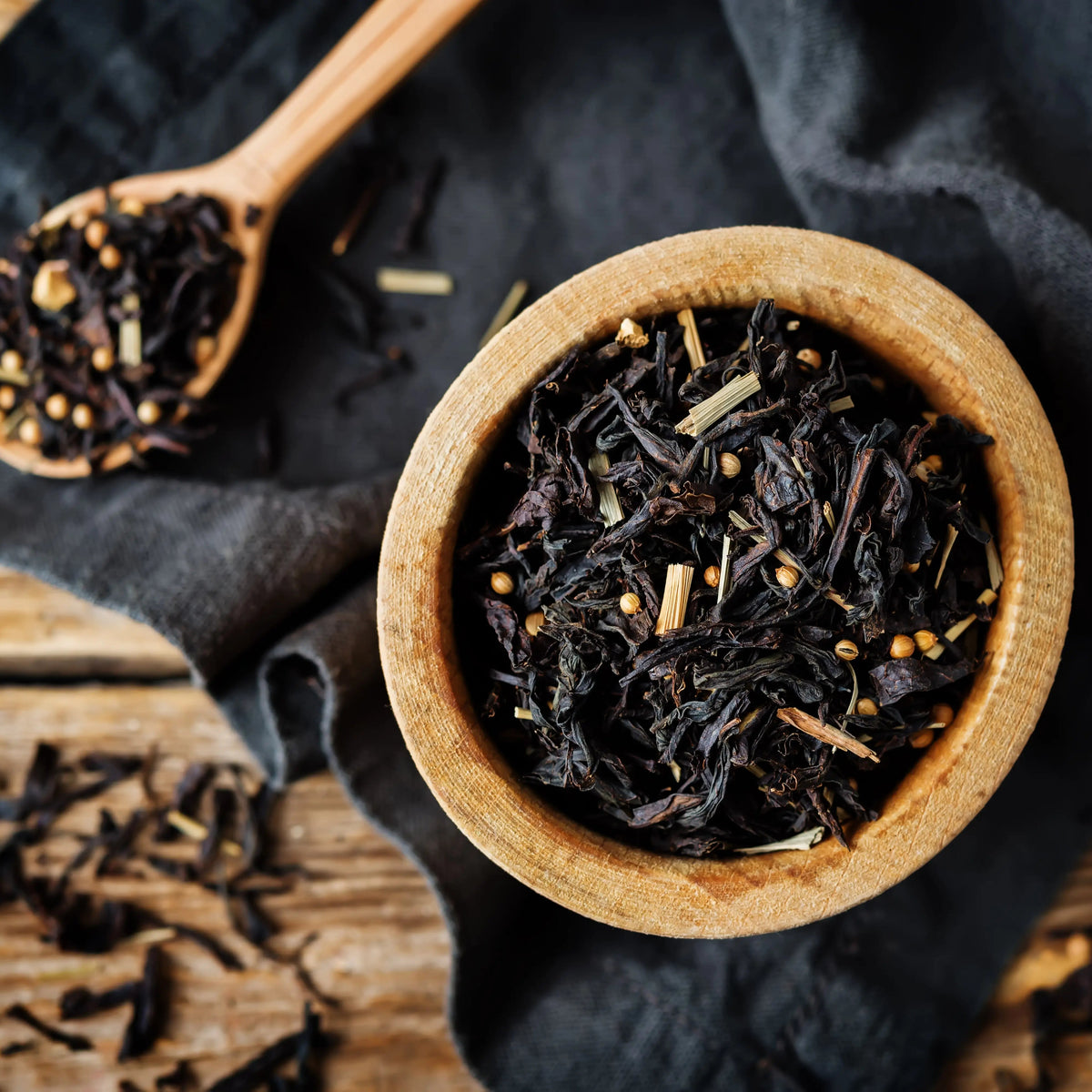 Wooden bowl of loose leaf tea and botanicals on a black linen towel on a wooden table